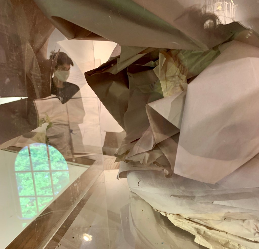 photo by Jovita Purqueras: me masked and a window, refelcted in my paper pile piece from DISTANCE at Cultural Arts Center (2020)